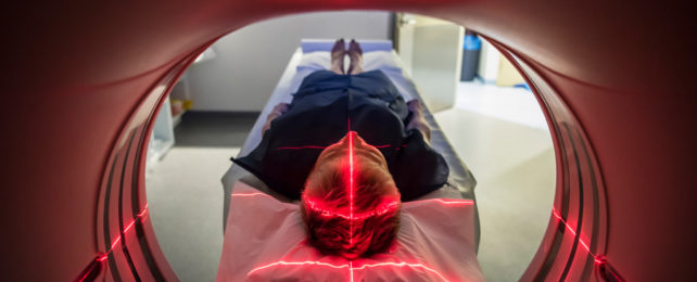 A person in an MRI machine, with red laser lights over the head.
